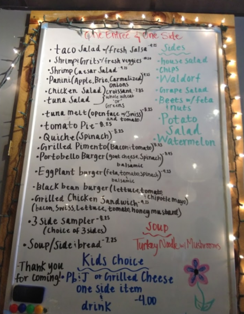 Menu board featuring various dishes like taco salad, panini, and eggplant burger, with prices and side options listed.