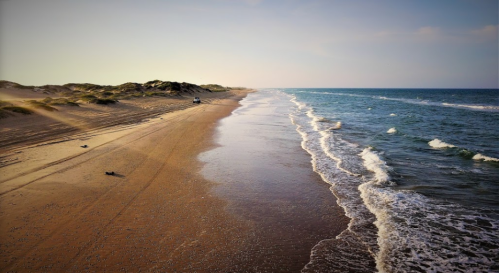 A serene beach scene with gentle waves, sandy shore, and distant figures walking along the coastline under a clear sky.