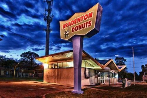 A retro donut shop sign at dusk, with a colorful sky and a quiet parking lot in Bradenton.
