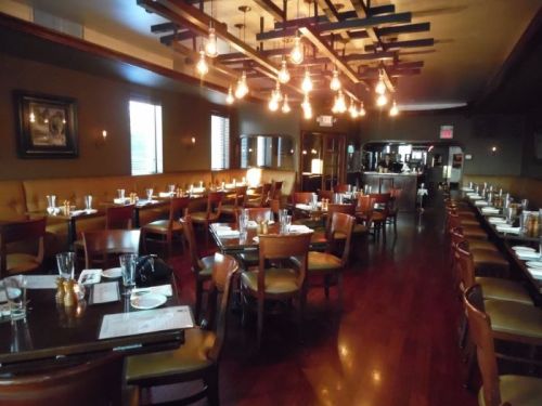 A warmly lit restaurant interior with wooden tables, chairs, and a cozy atmosphere, ready for dining.