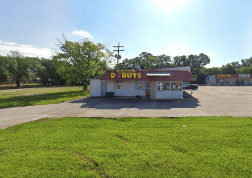 A small donut shop with a bright sign, surrounded by green grass and a clear blue sky.