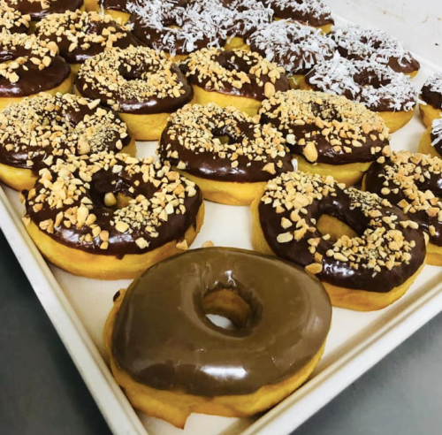 A tray of assorted donuts topped with chocolate icing, nuts, and shredded coconut.