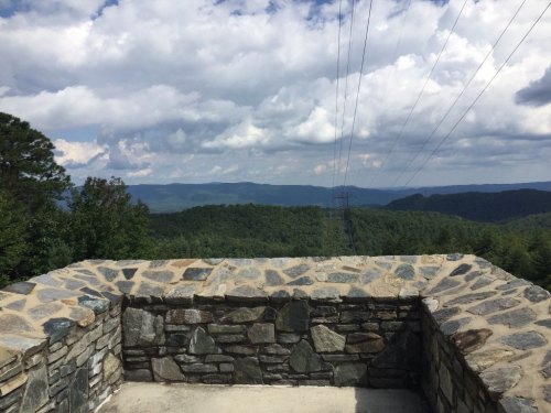 A stone overlook with a view of rolling green mountains and a cloudy sky in the background.