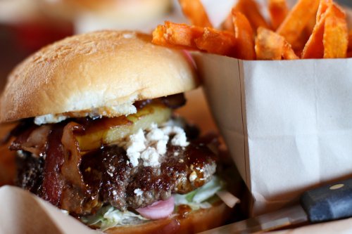 A juicy burger with bacon, lettuce, and toppings, served with a side of crispy sweet potato fries.