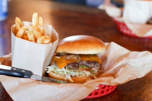 A juicy cheeseburger with lettuce and pickles, served with a side of crispy fries in a red basket.