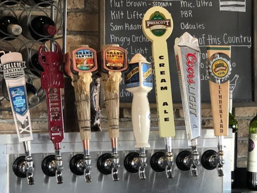 A row of beer taps featuring various craft beers with colorful labels against a brick wall backdrop.