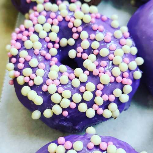 A purple frosted donut topped with pink and white sprinkles, resting on a light surface.