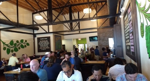 A busy restaurant interior with patrons dining, wooden tables, and green wall decor.