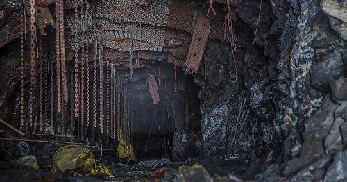 A dark, abandoned mine tunnel with rusty chains and metal debris hanging from the ceiling, surrounded by rocky walls.
