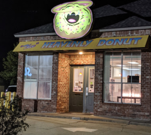 A brightly lit donut shop at night with a neon donut sign and a welcoming entrance.