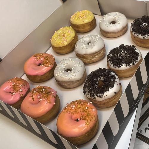 A box of assorted donuts with colorful icing and toppings, including pink, yellow, and white varieties.