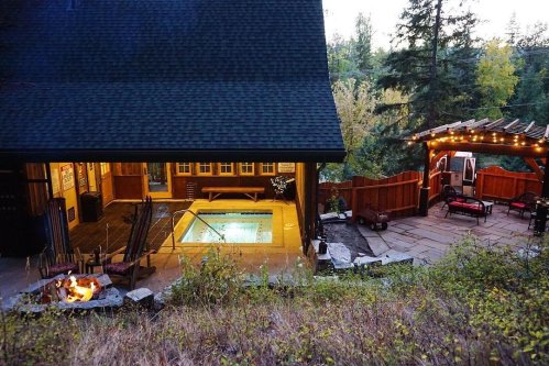 A cozy outdoor space featuring a hot tub, fire pit, and seating area, surrounded by trees and a rustic cabin.