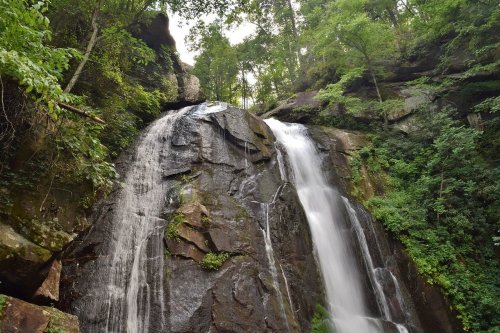 A cascading waterfall flows down rocky cliffs, surrounded by lush green trees and foliage.