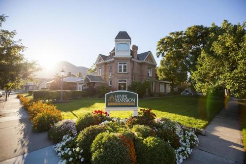 Historic Hines Mansion surrounded by colorful flowers and greenery, with sunlight illuminating the scene.