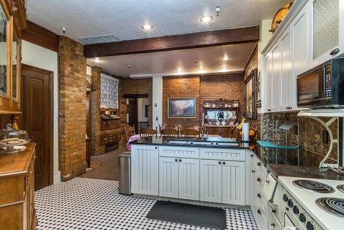 A spacious kitchen featuring white cabinets, a black countertop, and a patterned tile floor, with exposed brick walls.