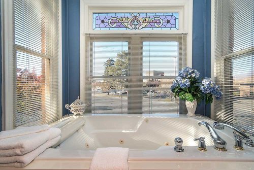 A luxurious bathtub with white towels, a decorative vase, and a stained glass window, surrounded by natural light.