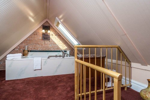 Cozy attic space featuring a bathtub, brick wall, and a small staircase, with warm lighting and plush carpet.