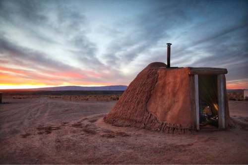 A traditional adobe structure at sunset, with a chimney and a colorful sky in the background.