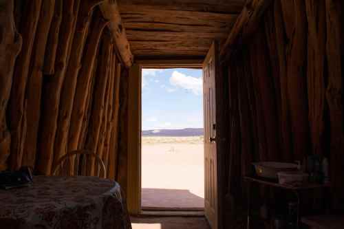 View from inside a rustic wooden structure, looking out at a desert landscape and blue sky through an open door.