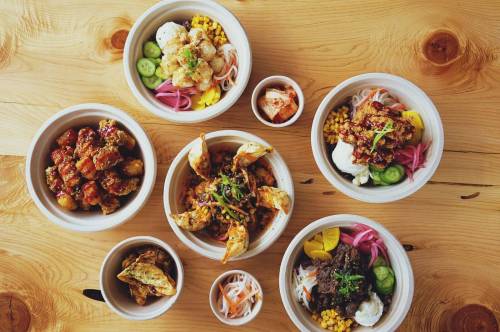 A variety of colorful dishes in bowls, featuring seafood, vegetables, and garnishes, arranged on a wooden table.