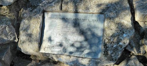 Plaque on a rock commemorating Prairie Creek Park Falls, detailing its history and significance from 1993.