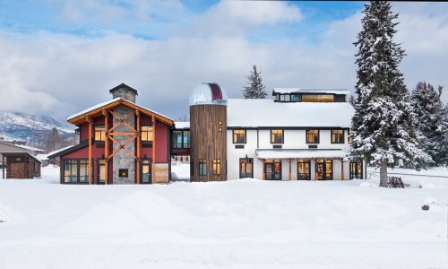 A modern, multi-story building with a mix of wood and metal exteriors, surrounded by snow-covered ground and trees.