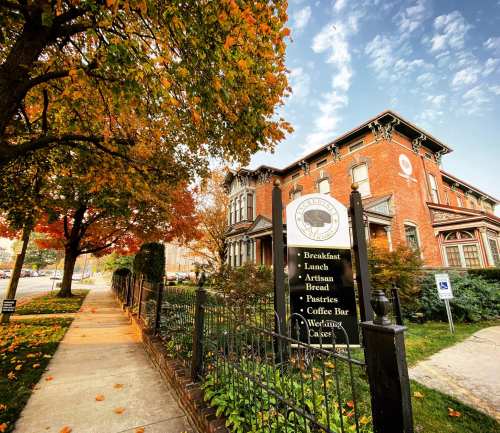 A charming brick building with a sign for breakfast and lunch, surrounded by colorful autumn leaves and a sidewalk.