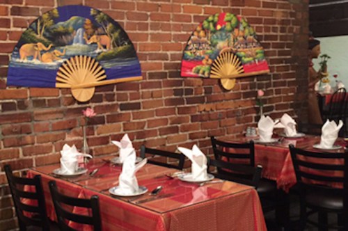 Cozy restaurant interior with brick walls, decorated fans, and neatly set tables with white napkins and dishes.