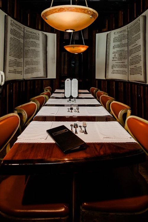 A cozy restaurant interior with a long table set for dining, featuring large menus and warm lighting.