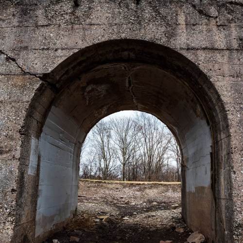 View through a weathered archway, revealing bare trees and a cloudy sky in the background.