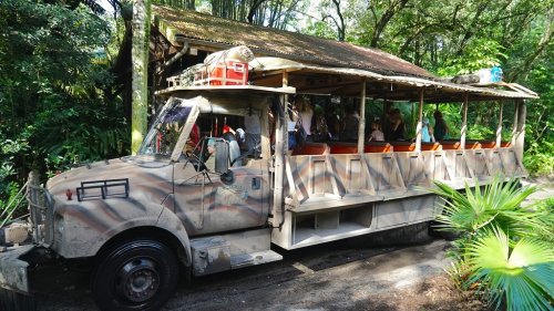 A safari-style truck with open seating parked in a lush, green jungle setting.