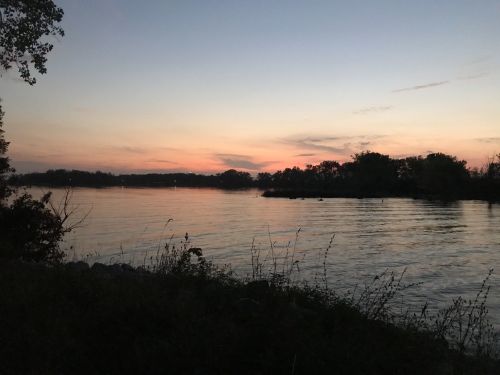 A serene river at sunset, with soft colors reflecting on the water and silhouettes of trees along the shore.