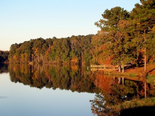 A serene lake surrounded by trees reflecting autumn colors in the water under a clear sky.