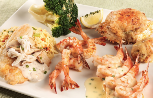 A plate featuring grilled fish, shrimp, crab, rice, broccoli, and lemon, arranged appetizingly.