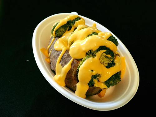 Baked potato topped with broccoli and drizzled with melted cheese sauce, served in a white dish.