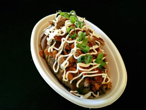 A bowl of pulled pork topped with green onions and drizzled with barbecue sauce and mayonnaise on a black background.