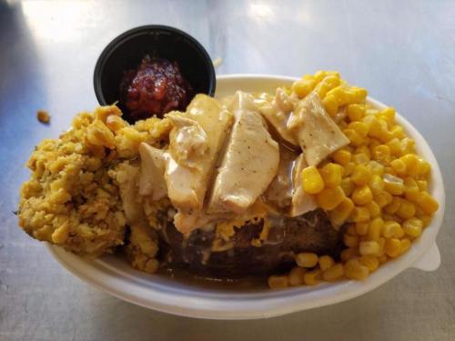 A plate of food featuring sliced turkey with gravy, corn, stuffing, and a side of sauce in a small cup.
