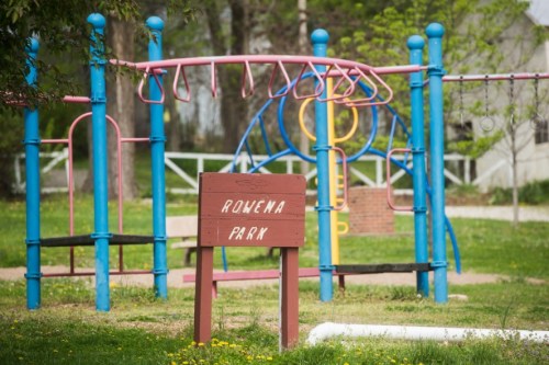 A playground with colorful equipment and a sign reading "Rowena Park" in a grassy area.