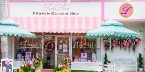 A charming macaron shop with pink awnings, outdoor seating, and floral decorations.