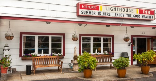 Exterior of the Historic Lighthouse Inn, featuring benches, flower pots, and a sign promoting summer enjoyment.