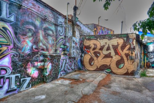 Colorful street art featuring a large face mural and bold graffiti text on a weathered urban wall.