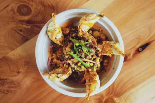 A bowl of colorful food featuring crispy wontons, mixed vegetables, and garnished with green herbs on a wooden table.