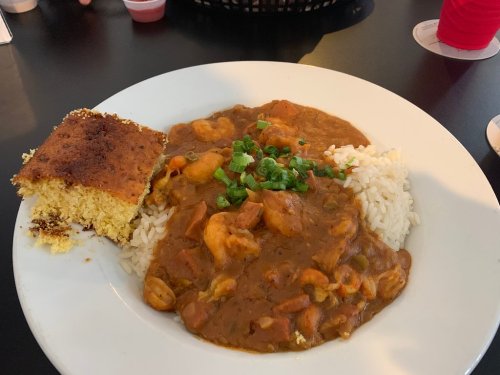 A plate of shrimp gumbo served over rice, garnished with green onions, alongside a piece of cornbread.