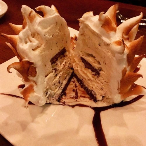 A beautifully presented dessert featuring a meringue-topped ice cream cake, sliced to reveal layers inside.