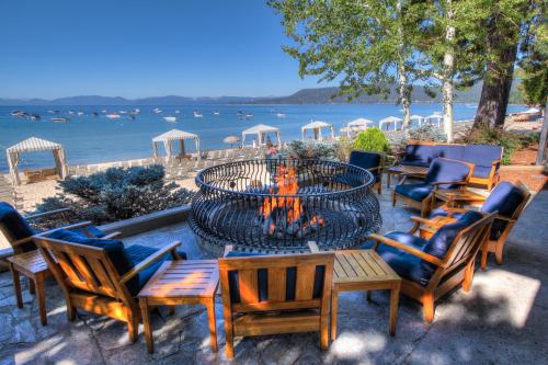 A cozy fire pit surrounded by wooden chairs, overlooking a beach with boats and cabanas under a clear blue sky.