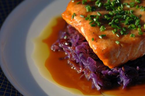 A piece of salmon topped with chives, served on a bed of purple cabbage with a drizzle of sauce.