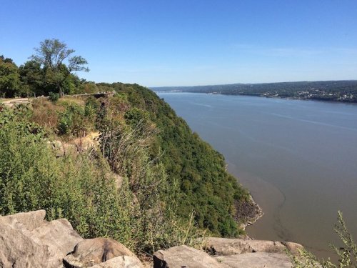 A scenic view of a river winding through lush green hills under a clear blue sky.