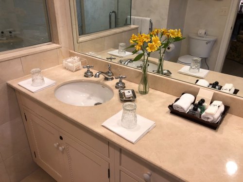 A clean bathroom countertop with a sink, flowers, towels, and toiletries arranged neatly.