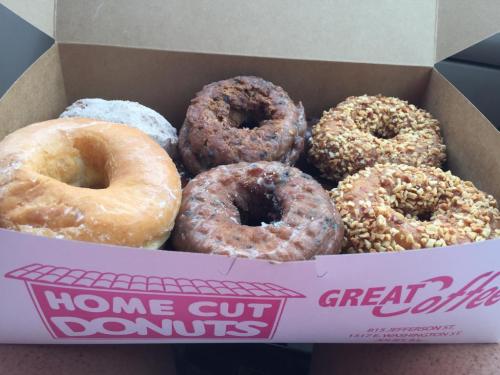 A box of assorted donuts, including glazed, chocolate, and nut-covered varieties, with a coffee shop logo.