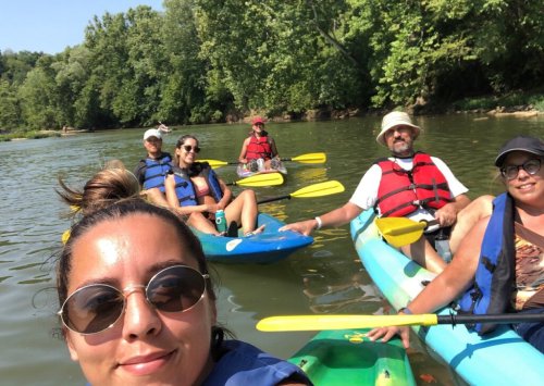 A group of six people kayaking on a river, enjoying a sunny day surrounded by greenery.